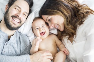 A Mother father and baby child on a white bed.